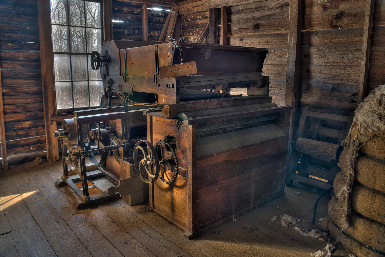An old wooden cotton gin with a stack of pressed bales beside it